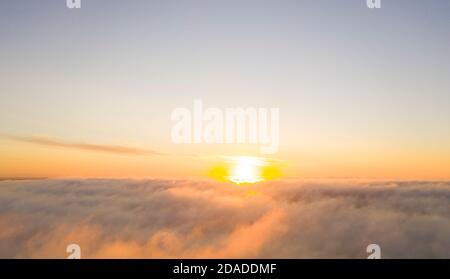 Aerial view gold sunrise over clouds in blue sky. Aerial top view cloudscape. Texture of clouds. View from above. Orange sunrise or sunset over clouds Stock Photo