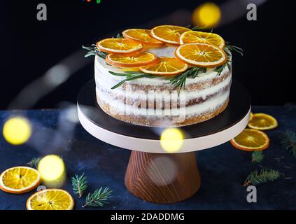 Beautiful delicious cake with sprigs of rosemary and orange frips. Delicious New Year's dessert. Biscuit cakes, curd cream, gingerbread. Stock Photo
