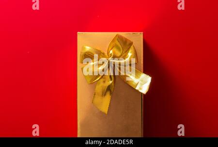 Gift in a golden package with a bow on a red background Stock Photo