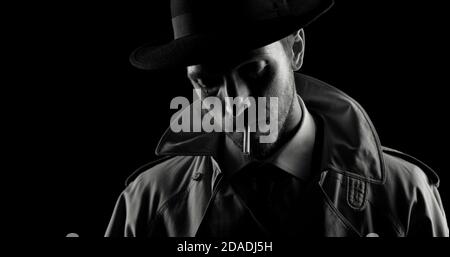 Noir film detective posing in the dark, he is smoking a cigarette Stock Photo