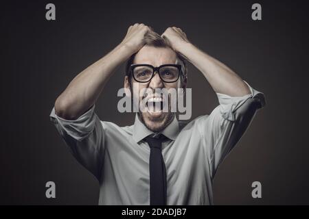 Angry stressed businessman with head in hands, he is shouting and feeling frustrated Stock Photo