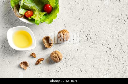 A white bowl with walnut oil with unique flavor, several walnuts and fresh salad on a gray background, top view with copy space Stock Photo