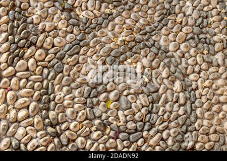 background texture of laid out mosaic pebbles. The texture of the stone wall, the road from small round and oval stones with abstract lines laid out p Stock Photo