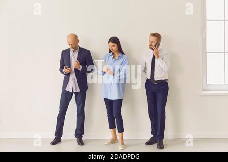 Serious busy multiethnic people of different ages using modern gadgets while waiting in line Stock Photo
