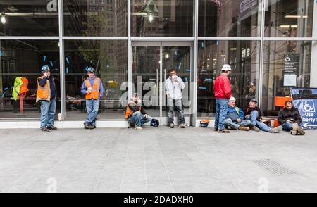 NEW YORK, USA - Apr 28, 2016: Group of construction workers having a break on site in Lower Manhattan. Drinking coffee, talking by phones and sitting Stock Photo