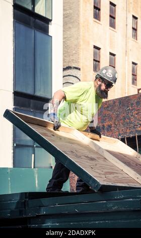 NEW YORK, USA - Apr 30, 2016: Worker with a beard and a tattoo on his arm at the construction site of the Lower Manhattan working with plywood panels. Stock Photo
