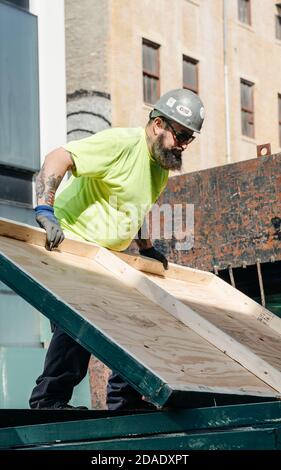 NEW YORK, USA - Apr 30, 2016: Worker with a beard and a tattoo on his arm at the construction site of the Lower Manhattan working with plywood panels. Stock Photo