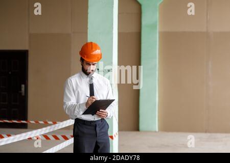 A young bearded Architect in a construction helmet on a construction site checks the result Stock Photo