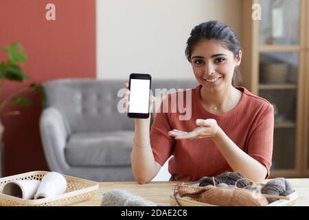 Portrait of young woman smiling at camera and pointing at her mobile phone she using online program in her work Stock Photo