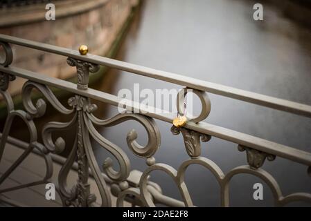 Wedding castle in the shape of a heart on the bridge. Golden castle on a metal fmgurny fence against the background of the river. Stock Photo