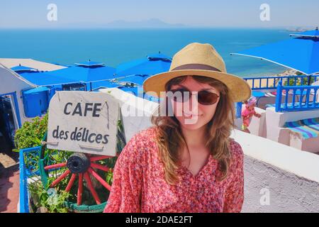 Girl stands outside an arab cafe des delices with blue umbrellas and white walls - Sidi Bou Said, Tunisia, 06 18 2019 Stock Photo
