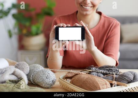 Close-up of young woman sitting at the table among wool threads and showing the empty screen of her mobile phone Stock Photo