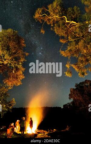 People stand around a campfire with the milky way above. Stock Photo