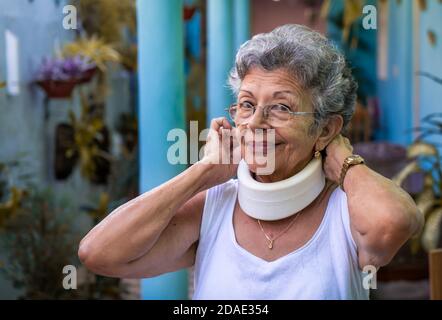 Smiling elderly woman putting on homemade looking cervical immobilizer collar Stock Photo