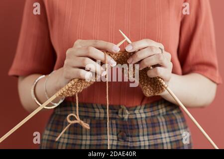 Close-up of woman knitting scarf from yarn standing against the pink background Stock Photo