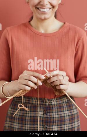 Close-up of young woman smiling at camera doing needlework while standing against the pink background Stock Photo