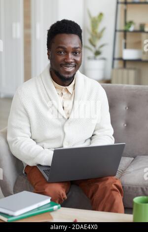 Portrait of African young man smiling at camera while sitting on sofa and working on laptop Stock Photo