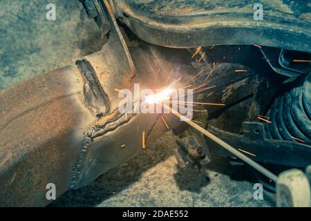Welder Welding Bottom Car Chassis by Electric Welding Torch on Top Left View in Vintage Tone Stock Photo
