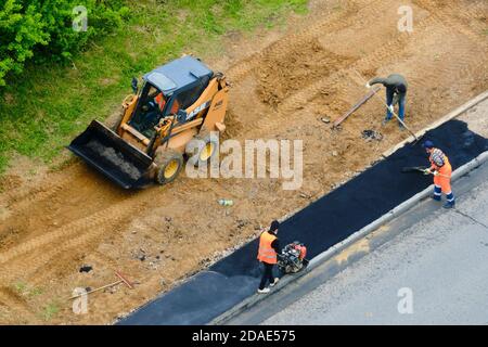 Road worker using a small bulldozer case and workers with shovels - Moscow, Russia, may 21, 2020 Stock Photo