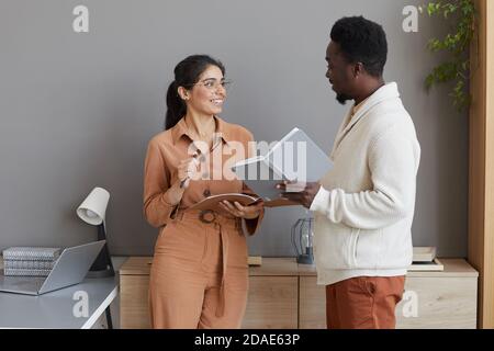 Business partners with notepads in their hands standing at office and discussing new plans Stock Photo
