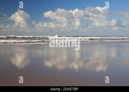 White fluffy clouds with reflections on Sandymouth beach Cornwall Stock Photo