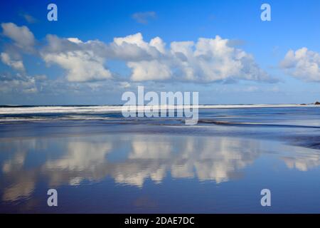 White fluffy clouds with reflections on Sandymouth beach Cornwall Stock Photo