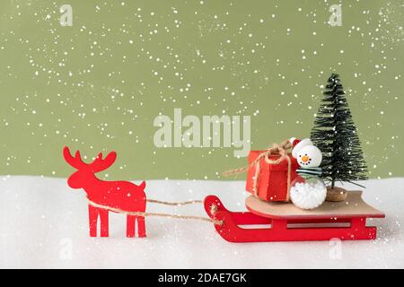 Toy reindeer and sleigh delivering Christmas present and tree on green background. Stock Photo