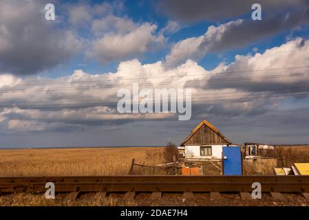 Blue cloudy sky above the reeds with small house. House in the middle of nowhere. Old house lost in the reeds. Stock Photo