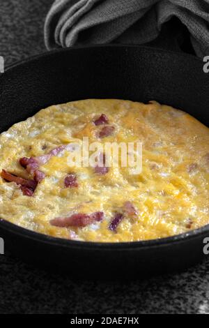 Omelette, with bacon, on a black granite surface in a cast iron frying pan.  Selective colour image Stock Photo