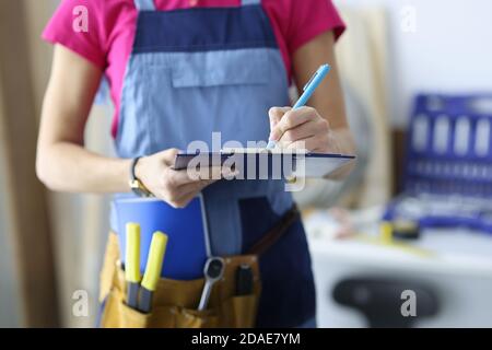 Woman builder in uniform writing with pen in document in workshop closeup Stock Photo
