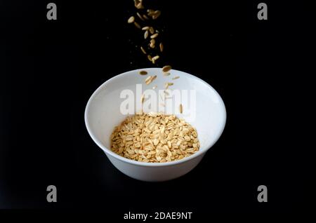 Oat flakes flying out of wooden bowl isolated on white and black background. Falling oats Stock Photo