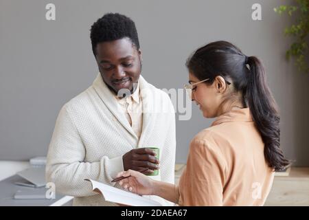 Young secretary pointing at documents and discussing them with African businessman at office Stock Photo