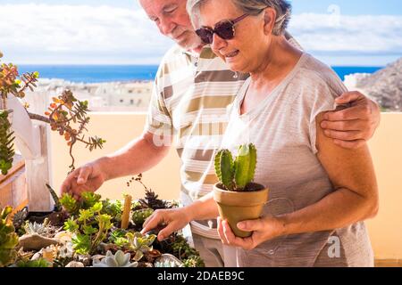 Elderly lifestyle with senior caucasian couple enjoying together a little garden at home inthe outdoor terrace - people and plants in gardening work having fun Stock Photo