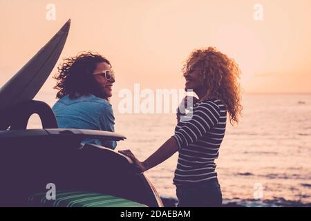 Cheerful and happy couple of women friends enjoying the sunset and travel together for vacation time - sea in background and young middle age enjoyed people near a car and surf table - concept of friendship and travel Stock Photo