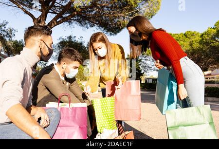 Group of young friends sitting on the steps of the square in the city wear face masks for protection against covid-19 coronavirus and look into their Stock Photo