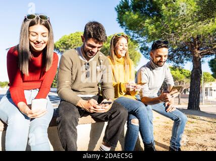 Two beautiful young couple sitting on a wall having fun using smartphone - Friends group smiling looking at the cell phone for chatting in social netw Stock Photo