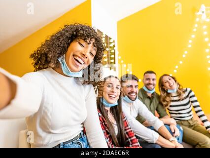 Group of multi ethnic young people having tech fun home - Beautiful black Hispanic woman take a photo with smartphone to her friends wearing lowered C Stock Photo