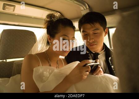 BEIJING, CHINA - JUNE 2006:  Li Xiao Ang, 26, company consultant and his bride-to-be  LI Yue, 27, who works in an advertising agency look through the pictures they took of each other during their photoshoots at Miracle Love wedding photo studio. T Stock Photo
