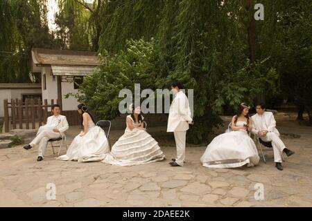BEIJING, CHINA - JUNE 2006:  Three couples who have been photographed in a Beijing park by Miracle Love wedding photo's photographers wait for a mini-bus back to the studio at the end of their session.g Stock Photo