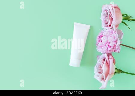 Mockup of white squeeze bottle plastic tube for branding of medicine or cosmetics. Cosmetic bottle container and light pink roses and peony on a green Stock Photo