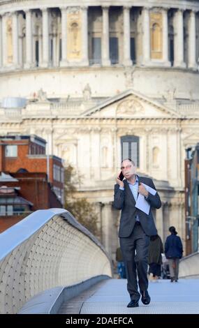 London, England, UK. Man walking over the Millennium Bridge, talking on his mobile phone, St Paul's Cathedral in the background Stock Photo