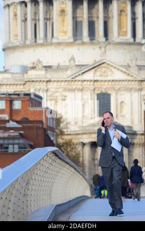 London, England, UK. Man walking over the Millennium Bridge, talking on his mobile phone, St Paul's Cathedral in the background Stock Photo