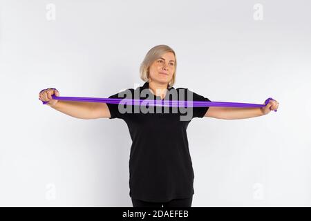Sporty senior woman on a white background stretches the fitness elastic band in her hands. Healthy lifestyle and pandemic concept. Stock Photo