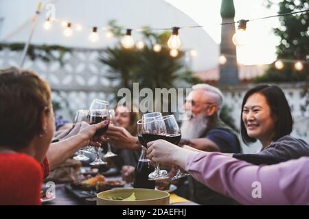 Happy family dining and tasting red wine glasses in barbecue dinner party - People with different ages and ethnicity having fun together Stock Photo