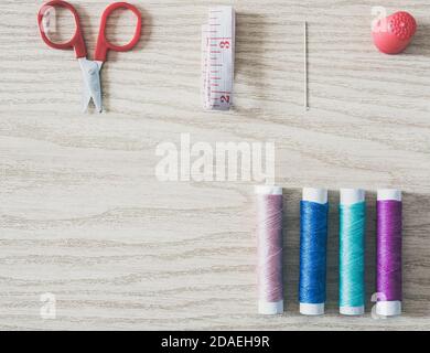 Spools of thread, bobbin, scissors and sewing accessories on a wooden background. Flatlay view. Stock Photo