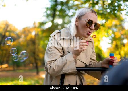 Mother blows soap bubbles to entertain baby in stroller Stock Photo