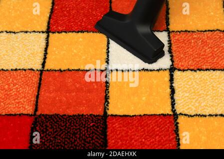 Vacuuming a rug with a pattern of colored squares. Fluffy carpet, interior element, floor covering is vacuum cleaned Stock Photo