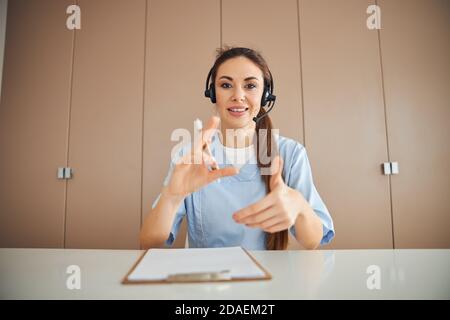 Beautiful female medic wearing headset and gesturing with her hands Stock Photo