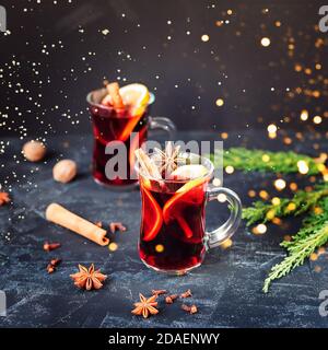Hot red mulled wine in glass with orange, cinnamon sticks, cloves and star anise on black background. Two spicy warm beverages. Seasonal Christmas mul Stock Photo