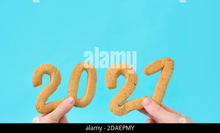 number 2021 of ginger cookies in women's hands on a blue background . festive new year background, template for greeting cards. conceptual design, spa Stock Photo
